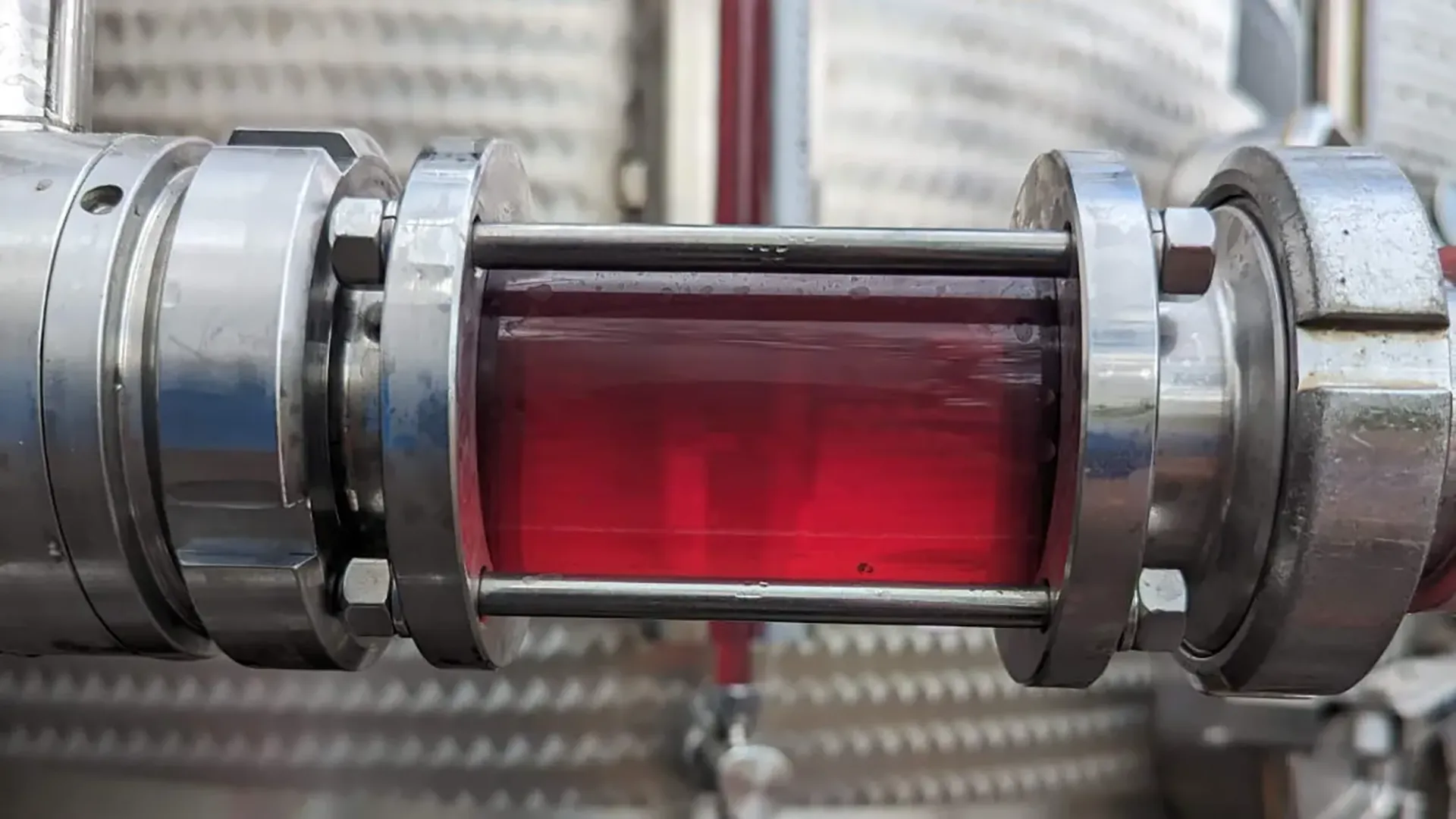 Tubo in acciaio con liquido rosso durante il processo di vinificazione in una cantina moderna.